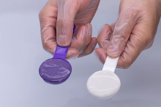 Two plastic measuring spoons holding purple and white PERFIT Putty dental impression material, demonstrating the two-component mixing system for precise dental impressions