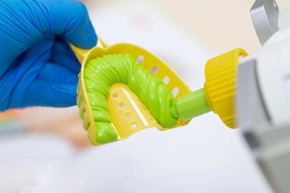 Dental impression of a green and yellow mold being filled with PERFIT Heavy Body-Auto Mix material using precision dispensing tool, demonstrating professional dental casting technique