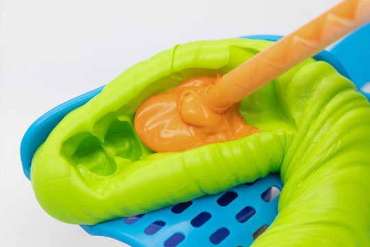 PERFIT Heavy Body-Auto Mix dental impression material being dispensed from nozzle into bright green mold with blue tray base, demonstrating material viscosity and flow properties