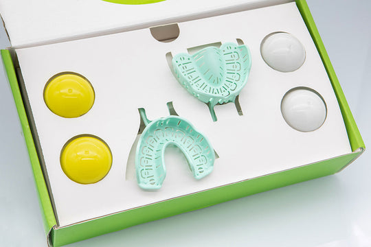 Dental Home Impression Kit with mint green dental trays, putty catalyst containers in yellow, and white impression material components in professional packaging for at-home teeth impressions