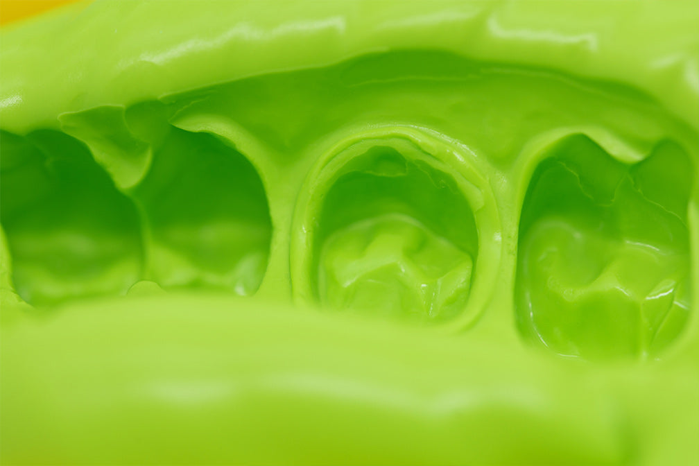 Detail macro shot of PERFIT Heavy Body-Auto Mix dental impression material in bright lime green color showing its smooth, viscous texture and distinct impression cavities formed for precise dental molds