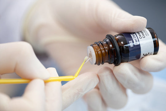 TopCEM-Ceramic Primer Ceramic Coupling Agent being precisely applied from small amber bottle using professional micro-applicator brush, demonstrating precise dental material application technique in clinical setting