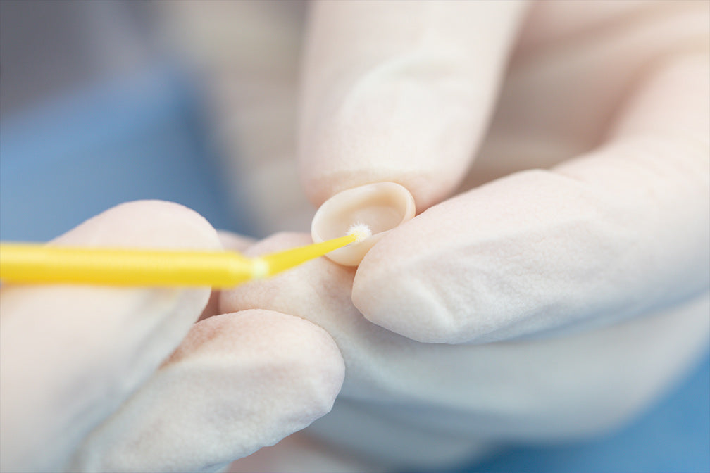 Professional application of TopCEM-Ceramic Primer Ceramic Coupling Agent using a micro brush applicator for dental restoration bonding, demonstrating precise dental material handling technique for optimal ceramic adhesion