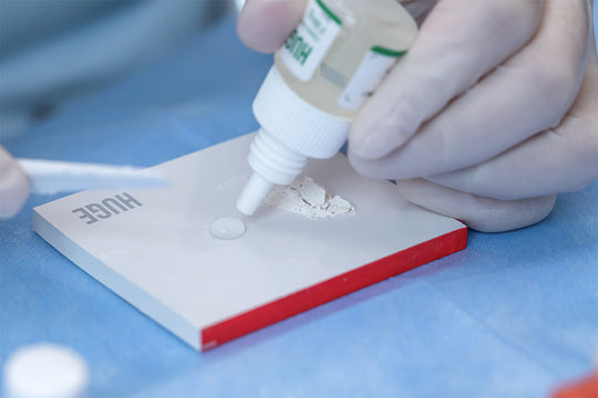 Professional applying Glass Ionomer Cement Filling I solution onto mixing pad, demonstrating proper dental material preparation technique with precise liquid dispensing for optimal dental restoration