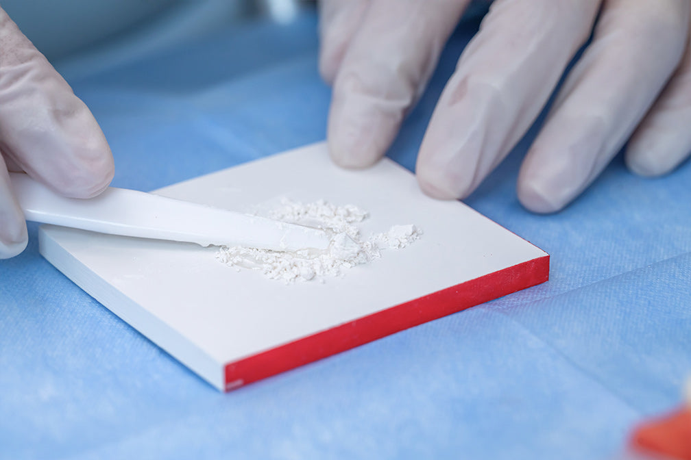 Dental professional mixing Glass Ionomer Cement Luting I powder on a red-edged mixing pad with gloved hands, demonstrating precise dental material preparation technique