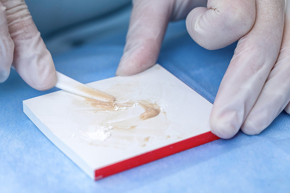 Dental professional mixing Glass Ionomer Cement Filling I material on a white mixing pad with precise technique, demonstrating proper powder-liquid ratio preparation for dental restoration procedure