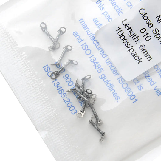 Dental Orthodontic Accessory Closed Coil Spring 0.010 6mm 10pcs/Bag displayed in clear packaging with product details visible. Small metal springs scattered on the package surface, showcasing the size and quantity of the orthodontic accessory.