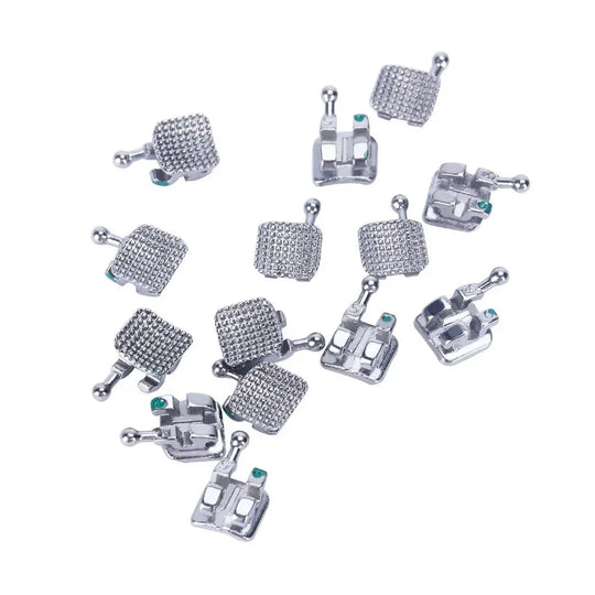 Dental Mini Metal Brackets Monoblock Roth .022/.018 Hooks on 345 20 Sets/Box displayed as multiple silver-colored orthodontic brackets with textured surfaces and small green markers, showcasing various angles and designs for dental applications