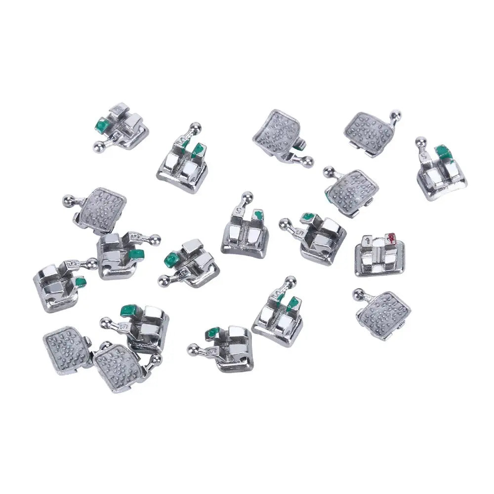 1000pcs Dental Metal Brackets Monoblock Mini Roth/MBT .022 Hooks On 345 scattered on white background. Silver orthodontic brackets with green and red markers visible. Various sizes and designs of brackets shown in disarray.