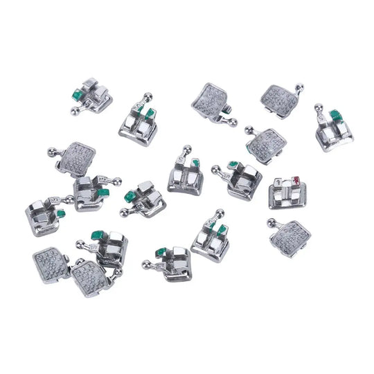 1000pcs Dental Metal Brackets Monoblock Mini Roth/MBT .022 Hooks On 345 scattered on white background. Silver orthodontic brackets with green and red markers visible. Various sizes and designs of brackets shown in disarray.