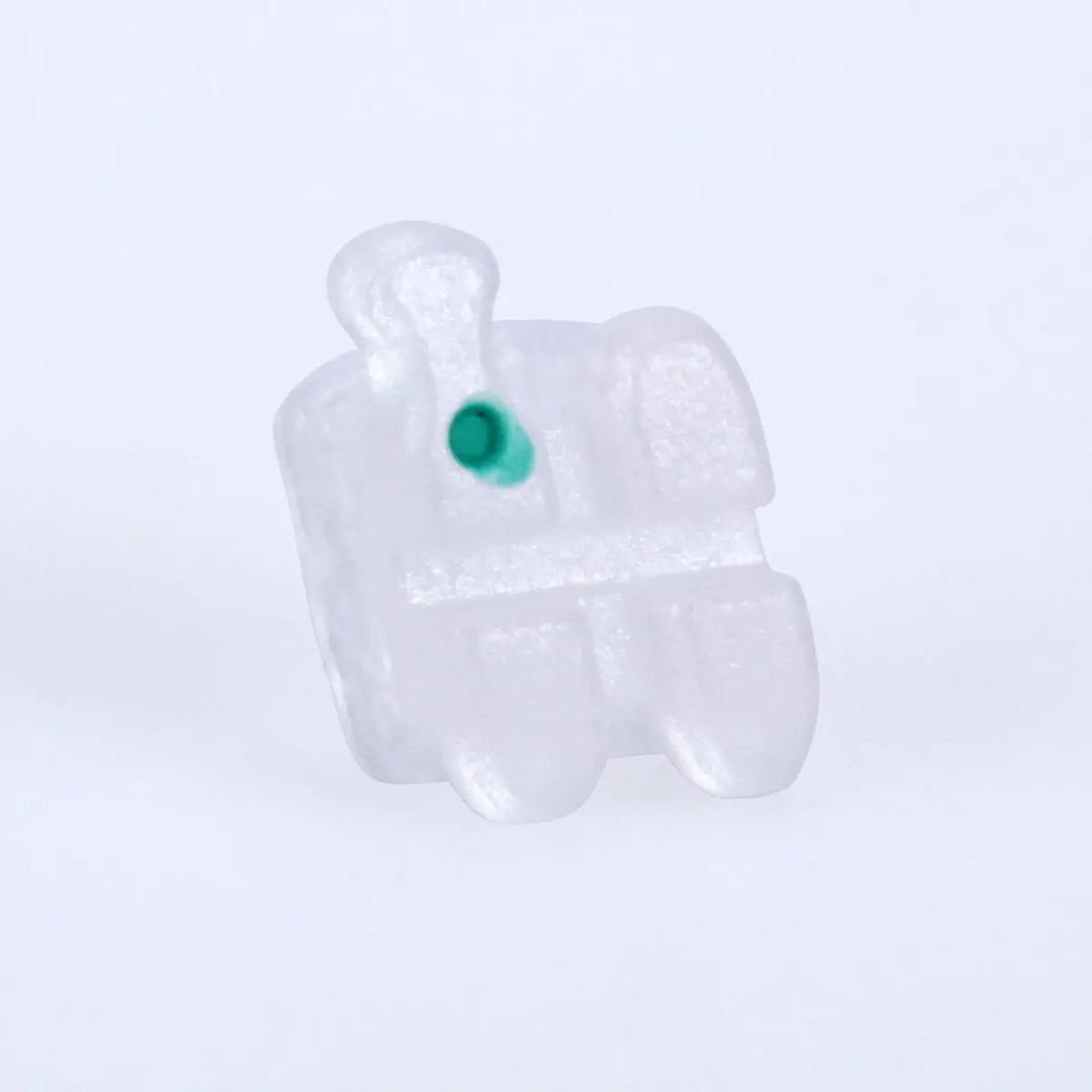 Ceramic Brackets Roth .018 Hooks 345 20pcs/Box: Close-up of a single transparent ceramic orthodontic bracket with a small green dot, showcasing its low-profile design and smooth edges for dental alignment and treatment