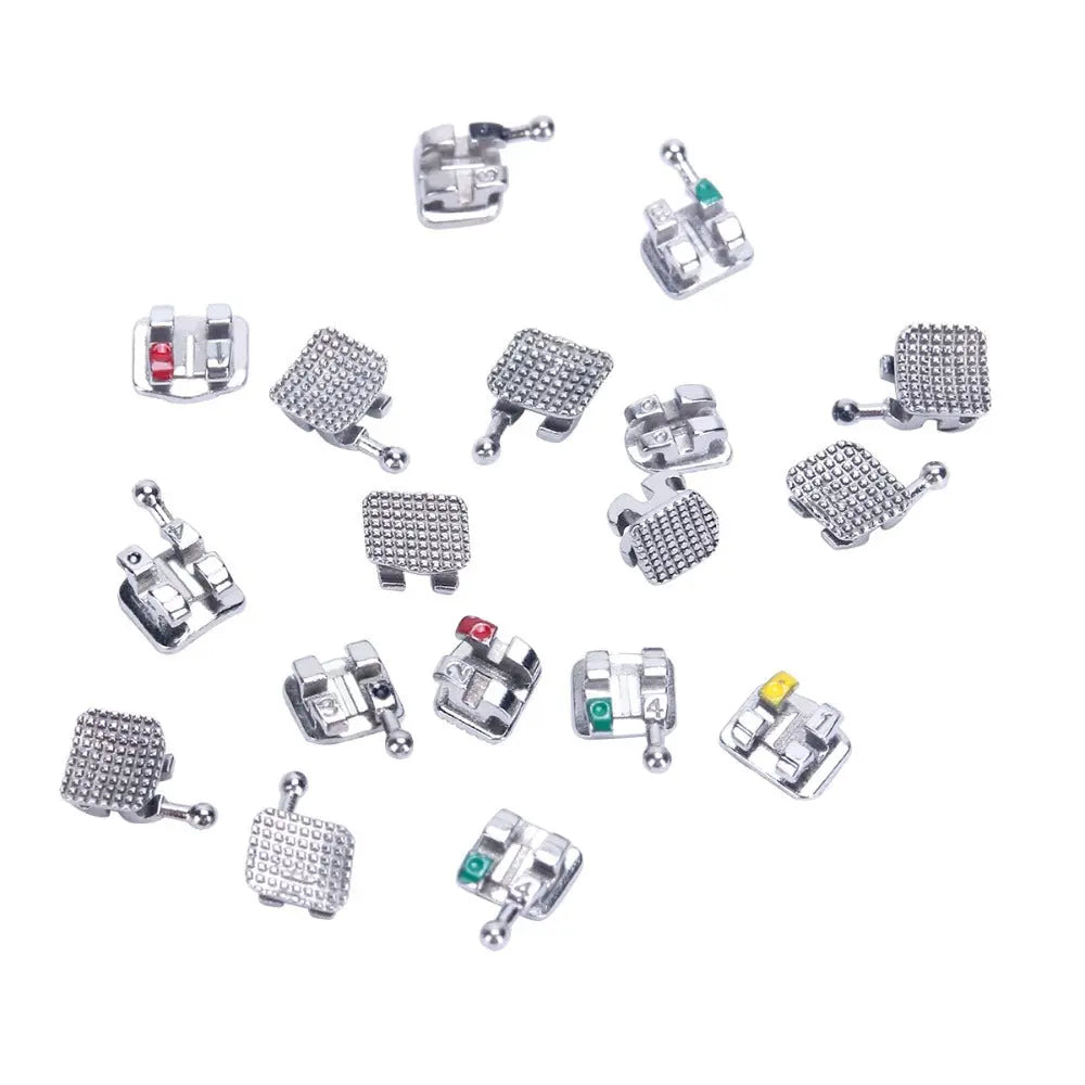 Dental Metal Brackets Mini Roth .018 MIM Monoblock Hooks on 345 400pcs/Box - Collection of various silver-colored orthodontic brackets with hooks and textured surfaces, displayed on a white background. Different designs and sizes visible, some with colored markings.