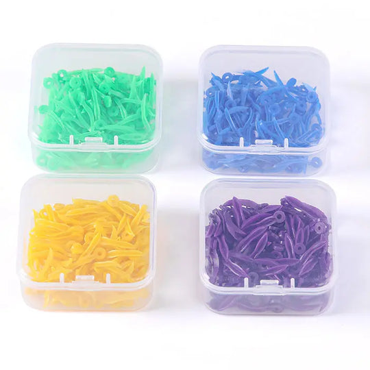 Dental Disposable Wedges With Hole Plastic Tooth Gap Wedge 4 Sizes 100pcs/Box: Four transparent boxes containing colorful plastic dental wedges in green, blue, yellow, and purple, each representing different sizes for various dental procedures.