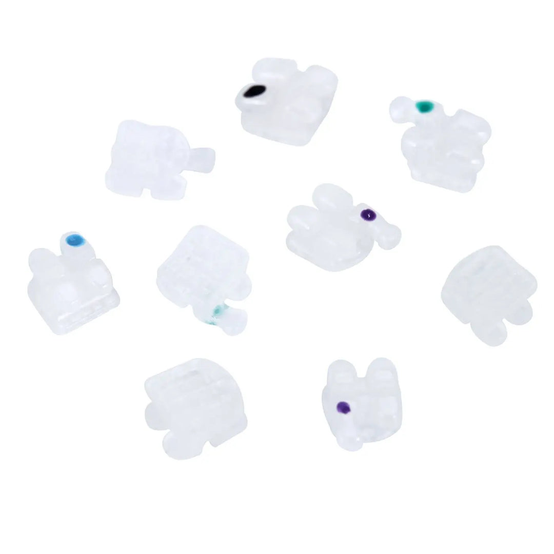 Dental Orthodontic Ceramic Brackets Full Size Hooks 345 20pcs/Box: Multiple white ceramic brackets with small colored dots, scattered on a white background, showcasing the product's design and variety for orthodontic use.