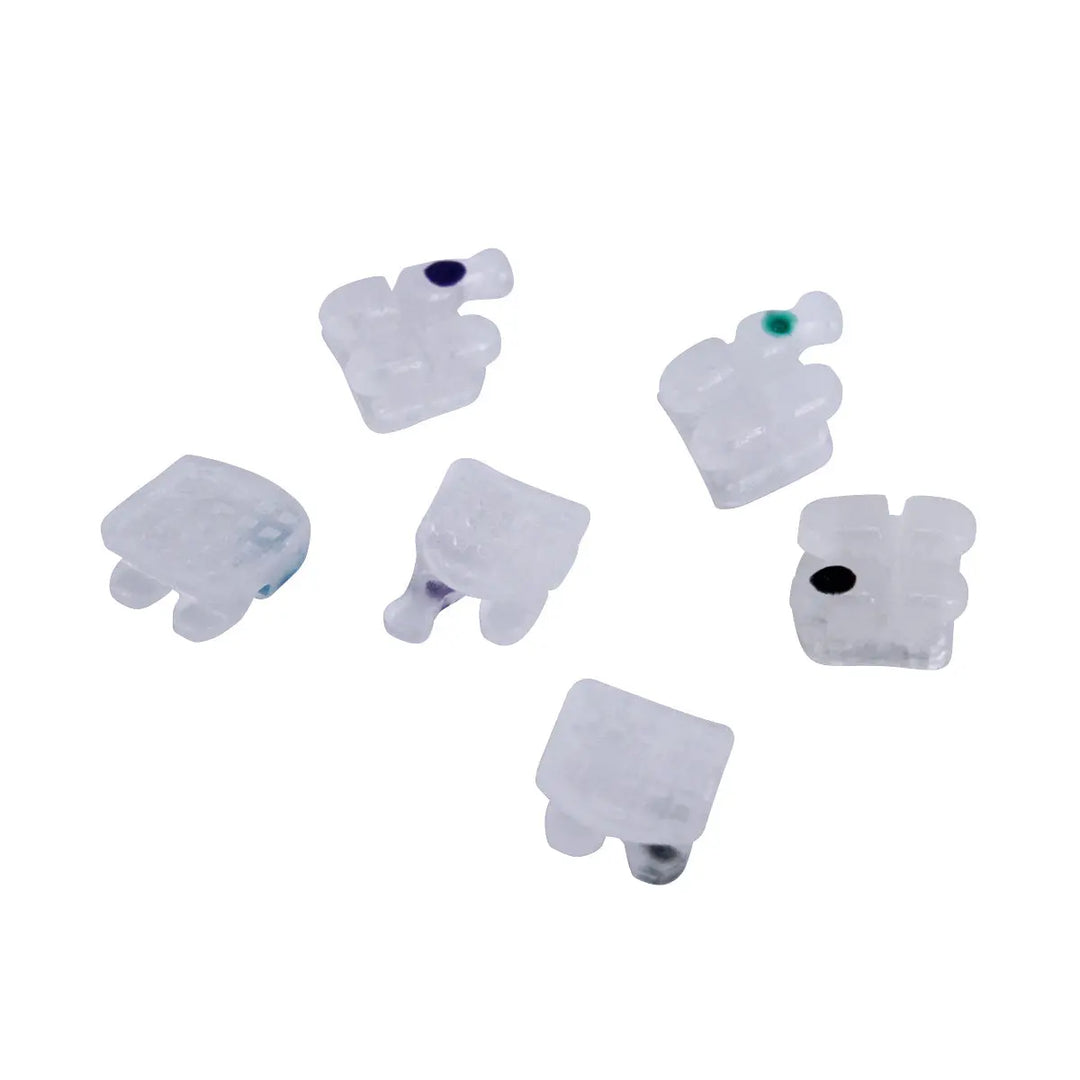 Ceramic Brackets Roth .018 Mesh Base 345/Hooks 20/Box: Six white ceramic orthodontic brackets with colored dots, showcasing low-profile design and mesh base for dental braces. Smooth, ergonomic shape for patient comfort and efficient tooth alignment.