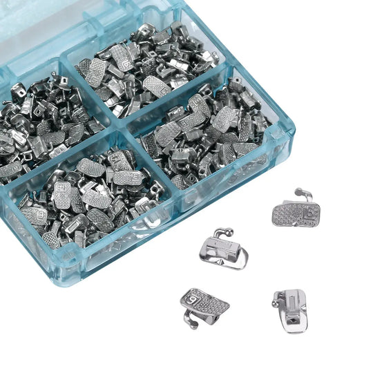 Buccal Tube 1st Molar Bondable Monoblock Non-convertible Roth 0.018 50Sets/Bx displayed in a blue plastic organizer box with compartments filled with small metal orthodontic components. Several individual buccal tubes visible outside the box, showing detailed metal structure.