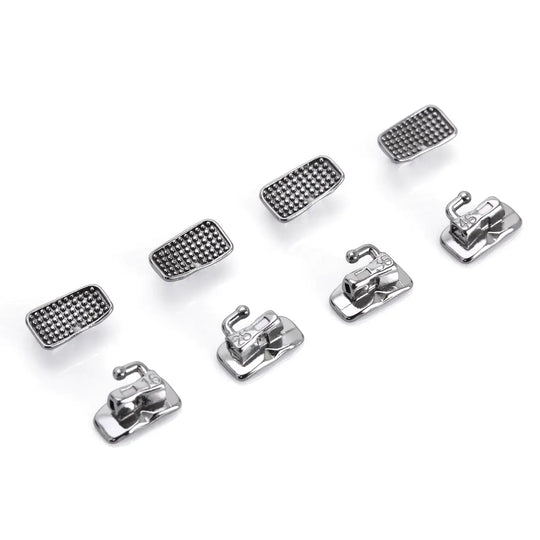 Buccal Tube 1st Molar Monoblock Non-Convertible Roth 0.018 50Sets/Bx - Close-up of eight metallic dental orthodontic components arranged in two rows, showing four textured rectangular pieces and four bracket-like structures with hooks, used for molar tooth alignment