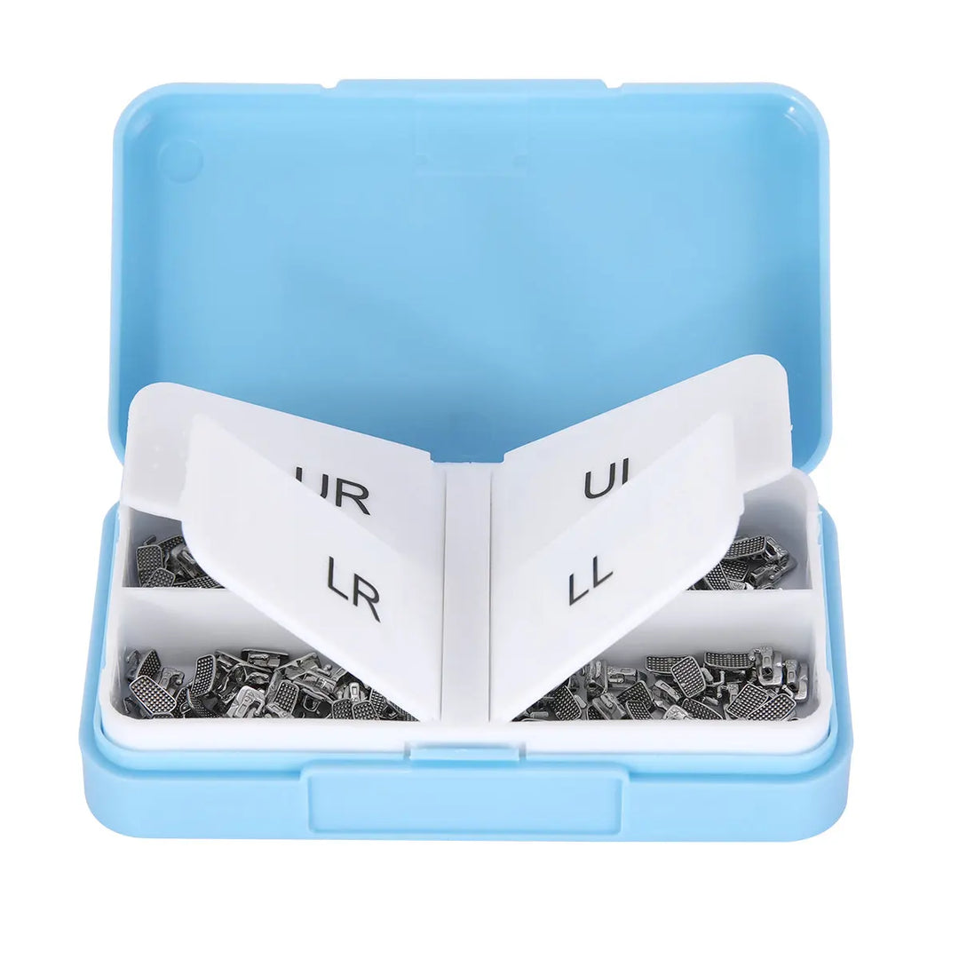 Buccal Tube 1st Molar Monoblock Non-Convertible Roth 0.018 50Sets/Bx in blue plastic case. Open box reveals white divider labeled UR, UL, LR, LL, with small metal orthodontic components visible in compartments. Dental orthodontic supplies neatly organized for professional use.