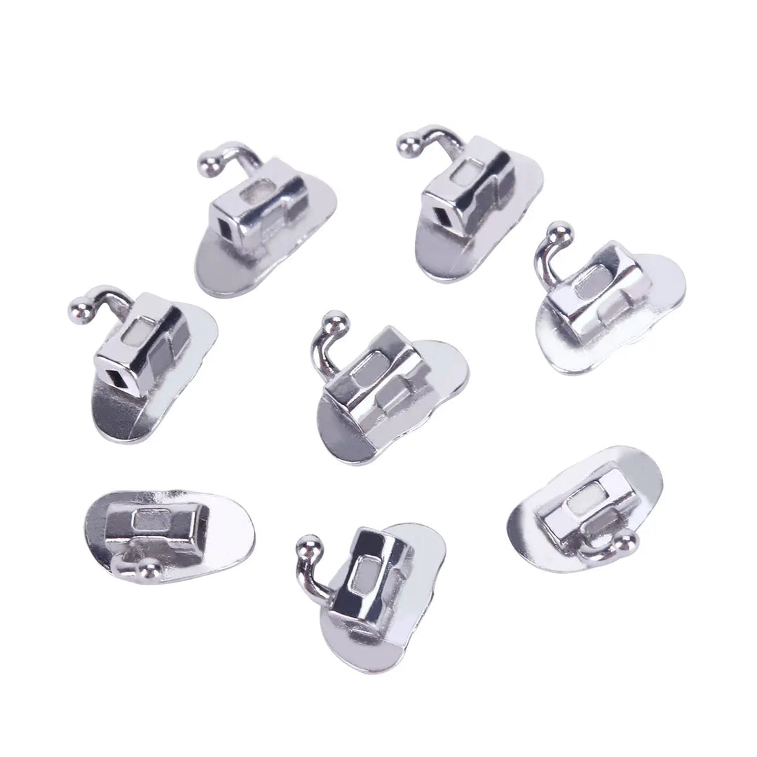 Buccal Tube 2nd Molar Bondable Monoblock Non-convertible Roth 0.022 20Sets/Bx - Dental orthodontic buccal tubes made of metal, shown in various angles. Small, silver-colored devices with curved hooks and flat bases for bonding to teeth. Used for attaching orthodontic wires to second molars.