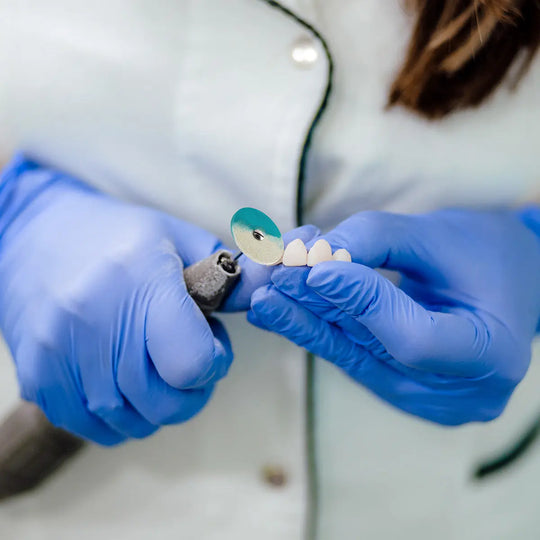 Dental Rubber Diamond Polisher Wheel Disc For Porcelain being used on dental prosthesis by gloved hands. Close-up of blue polishing disc on dental handpiece polishing artificial teeth, demonstrating product application for porcelain restorations.