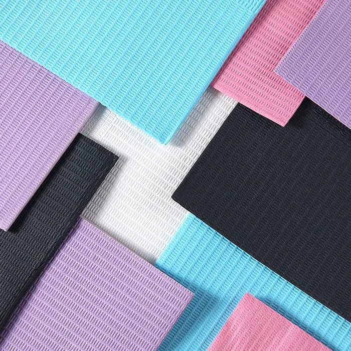 Colorful layers of disposable dental bibs in pastel blue, pink, purple, white, and black, showcasing the texture and variety of Dental Disposable Patient Bibs 13"x18" 2-Ply Paper/1-Ply Poly 125pcs/Pack.