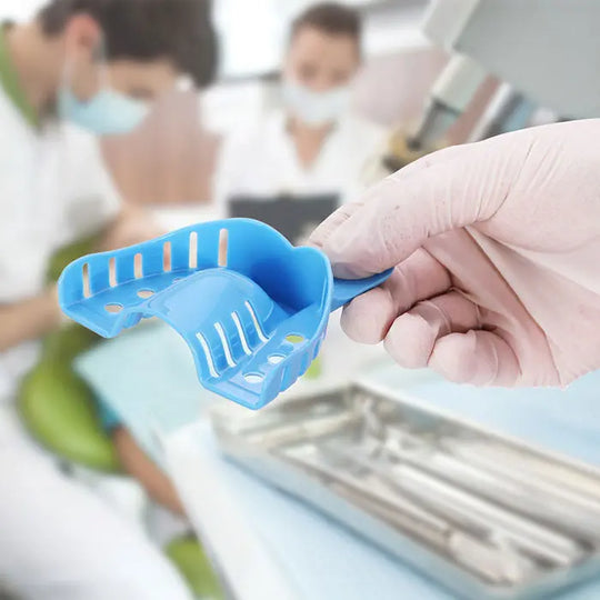 Blue perforated dental impression tray from Dental Impression Trays Kit held in dental office setting, showcasing ergonomic design and smooth surface for patient comfort. Part of 10-piece autoclavable plastic kit with various sizes.