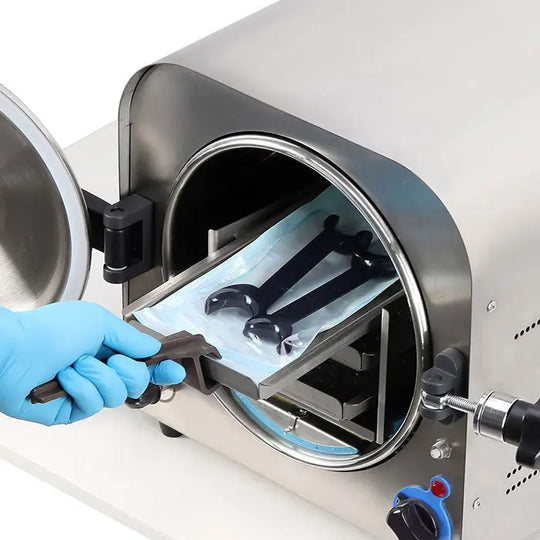 Dental T-Shape Double Head Cheek Retractors being sterilized in an autoclave machine. Gloved hand placing retractors inside stainless steel chamber, demonstrating dental equipment maintenance and hygiene practices for Shopify product listing.